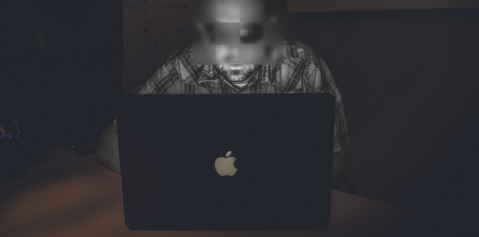 Technical Penguins Case Study: Cleaning Up After WordPress Hack. A man whose color has been changed to grayscale sits behind an open laptop, his face pixelated into a blur.