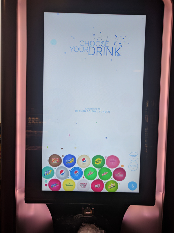 A touchscreen soda dispenser, with the accessibility mode enabled. The drink options are all the same size, arranged in rows along the bottom of the screen, where it would be easier to reach if someone were in a wheelchair.