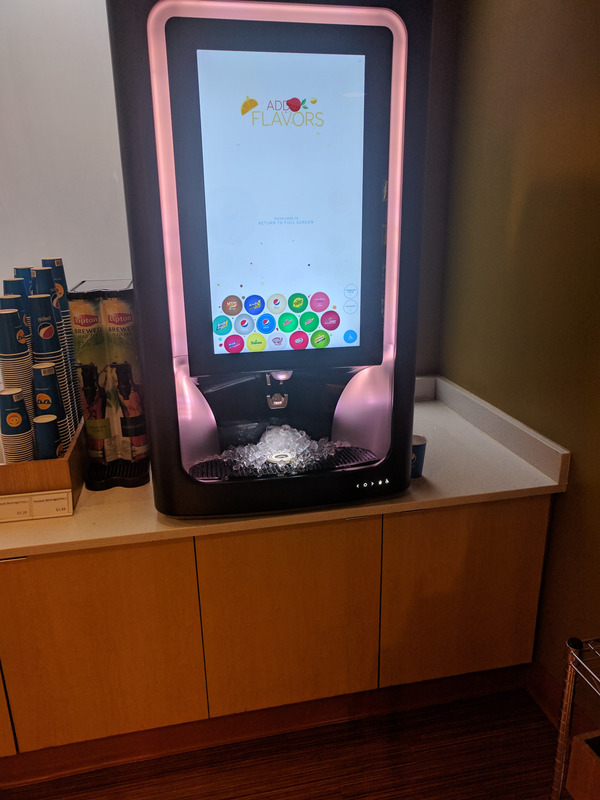 A wide shot of the touchscreen soda dispenser, showing its location on a three-foot-tall cabinet with no room underneath the dispenser for someone in a wheelchair to navigate to in order to be able to put a container under the nozzle.